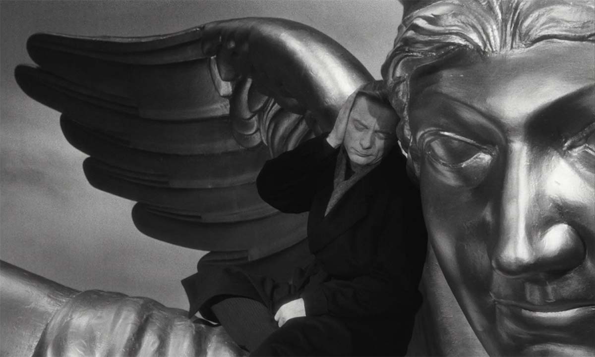 Photo of a main sitting on the shoulder of an enourmous angelic statue in the film Wings of Desire